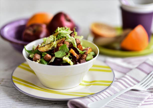 Πράσινη σαλάτα με ψητή τομάτα, σοταρισμένο μήλο και χοιρινό καπνιστό μπούτι σερβιρισμένη με ντρέσινγκ πορτοκαλιού